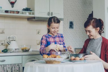 Little cute girl helping her mother in the kitchen stirring dough for cookies into bowl. Family, food, home and people concept