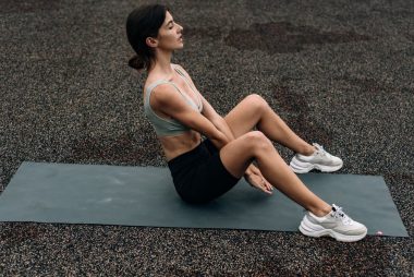 Woman sitting on yoga mat outdoors in an urban setting, embodying fitness and relaxation.